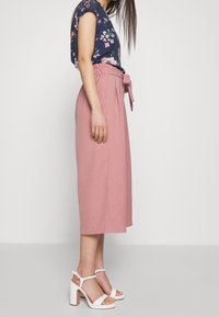 Floral navy top with short sleeves, paired with pink high-waisted culottes featuring a tied belt. Worn with white high-heeled sandals.