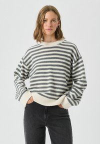Rayonowy sweter w kremowe i ciemnoszare paski, z okrągłym dekoltem, opuszczonymi ramionami oraz ściągaczami przy mankietach i dolnej krawędzi, w połączeniu z czarnymi dżinsami.
