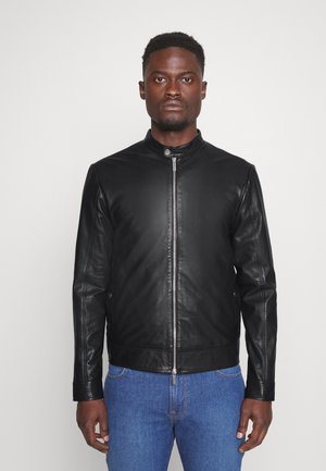 Black leather jacket with a stand collar and front zipper. Features a smooth texture and fitted design, paired with blue jeans.