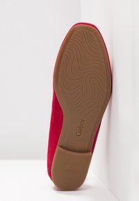 Chaussure en daim rouge avec un design incurvé et à enfiler. Dotée d'une semelle en caoutchouc texturé marron avec un motif ondulé et des détails de logo.