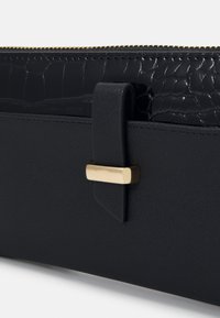 Sac à main noir en cuir lisse et mat avec un accent en texture crocodile, orné d'un fermoir en métal doré.