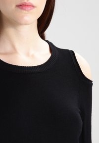 Czarny dzianinowy top z okrągłym dekoltem i wyciętymi ramionami. Dopasowany krój, gładka faktura i żebrowane akcenty przy dekolcie.