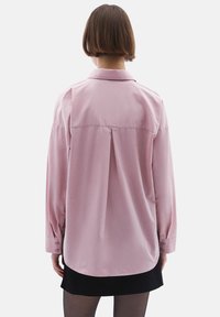Lichtroze blouse met lange mouwen en een plooidetail aan de achterkant, knoopsluiting bij de manchetten en een gebogen zoom. Soepele textuur, met een kraagontwerp.