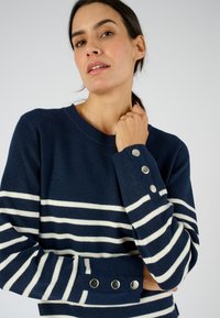 Maglione navy con strisce bianche, scollo rotondo e polsini decorati con bottoni. Morbida consistenza e vestibilità relaxed.