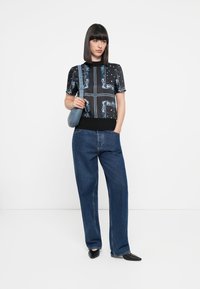 Black and blue patterned short-sleeve top with a ribbed hem, paired with wide-leg denim jeans and a small blue handbag. Black pointed shoes.