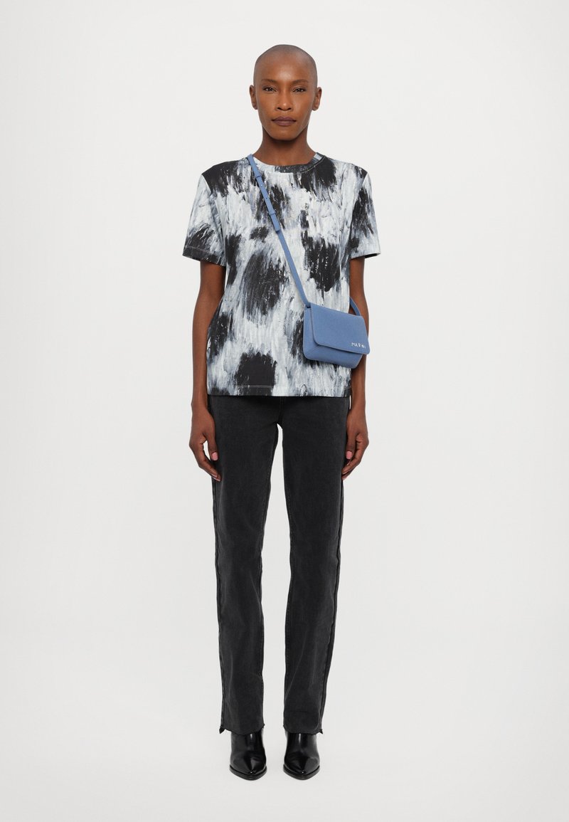 Chemise abstraite imprimée en noir et blanc à manches courtes, assortie à un jean noir. Les accessoires comprennent un petit sac à main bleu avec une bandoulière.