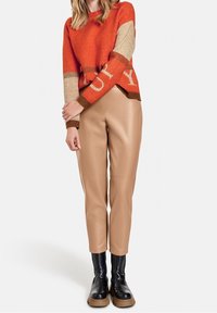 Stickad tröja i orange med beige accenter och fet skrift, kombinerad med beige byxor i falskt läder och svarta kraftiga ankelskor.