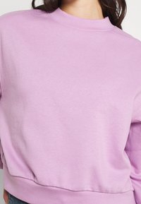 Sudadera lilas con cuello alto, hecha de un material suave. Presenta puños acanalados y un dobladillo ligeramente fruncido para un ajuste relajado.