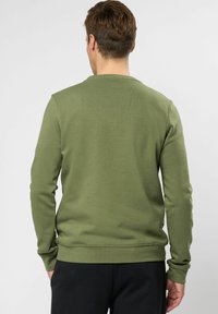 Olijfgroen sweatshirt met lange mouwen, geribbelde textuur en ronde hals. Heeft een getailleerde taille en boorden, naadloos ontwerp achterzijde.