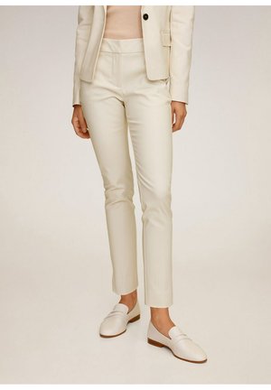 Cremefarbene, maßgeschneiderte Hosen aus glattem Stoff mit schmaler Passform und Seitentaschen, kombiniert mit weißen Loafers und einem hellen Oberteil.