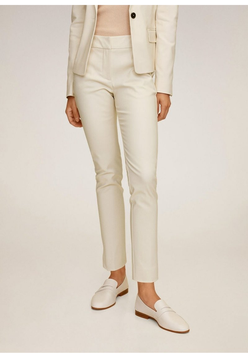 Pantalon sur mesure couleur crème en tissu lisse, coupe slim avec poches latérales, associé à des mocassins blancs et un haut léger.