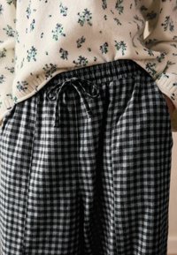 Fekete-fehér kockás nadrág rugalmas derékkal, húzózsinórral és zsebekkel. Az anyag lágy és könnyűnek tűnik.
