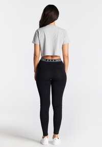Grå cropped t-shirt parret med sorte leggings med en mærket elastisk talje, båret med hvide sneakers. Glat stof og tætsiddende design.
