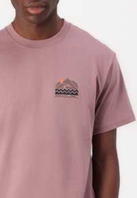 Kurzärmliges T-Shirt mit Rundhalsausschnitt aus rosa Baumwolle, das ein Grafikelement mit einem Berg und einer Welle in Dunkelgrau sowie einem orangefarbenen Sonnenelement zeigt.