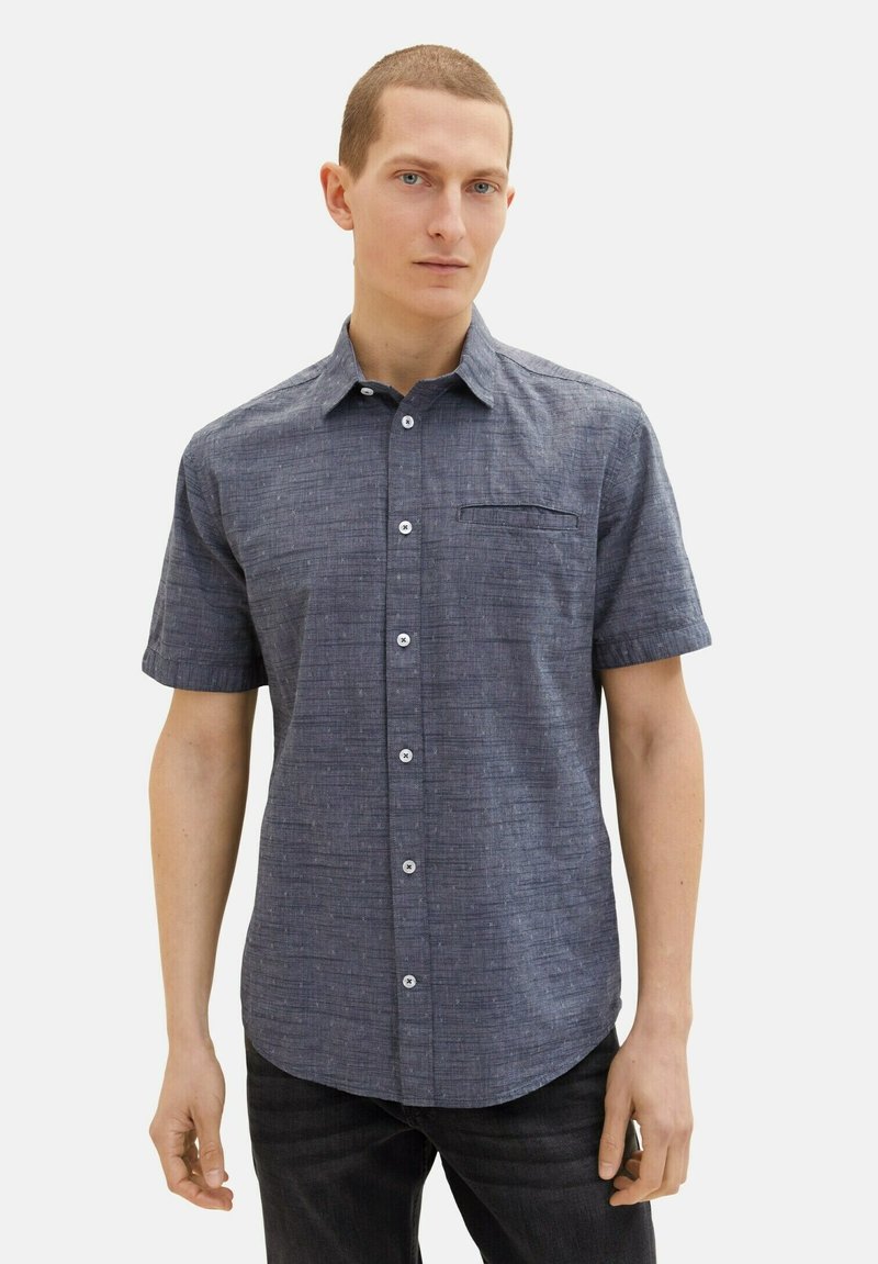 Kortärmad skjorta i strukturerad mörkblå tyg, med knäppning framtill, bröstficka och vita knappar.