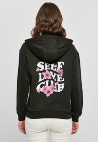 Felpa nera con una grande grafica bianca con la scritta "SELF LOVE CLUB", arricchita da illustrazioni floreali rosa. Miscela di cotone, vestibilità rilassata, tasche anteriori.