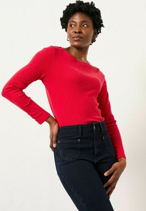 Rotes Langarmoberteil aus strukturiertem Material, kombiniert mit dunkelblauen, hoch taillierten Jeans mit Fronttaschen und goldfarbenen Akzenten.