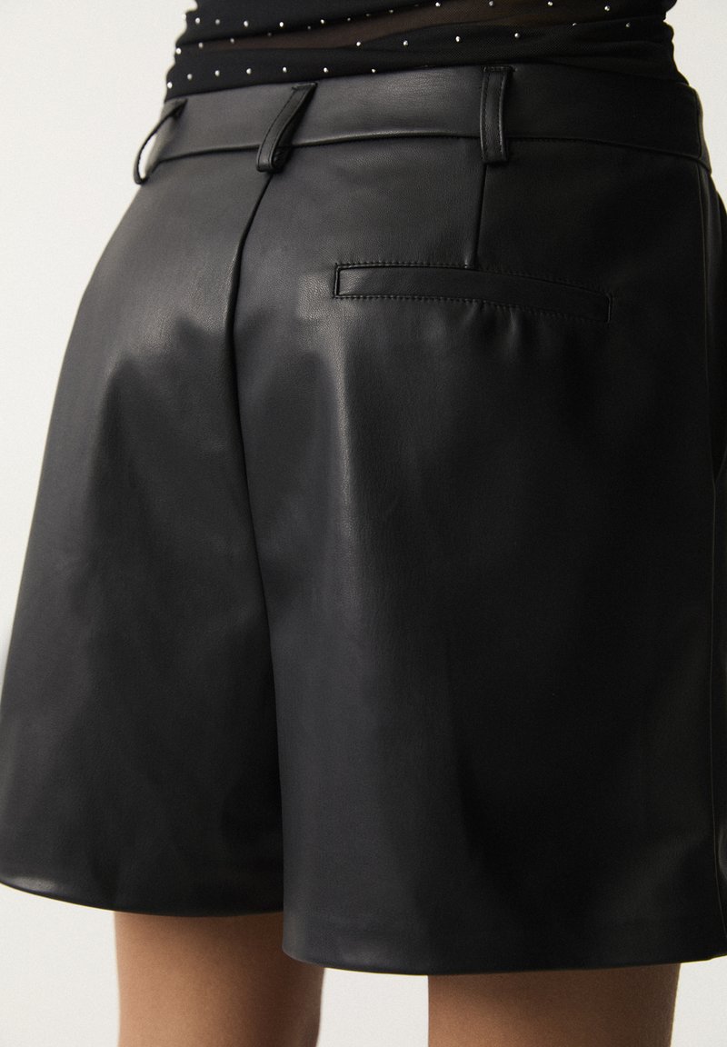 Pantaloni corti in pelle nera caratterizzati da una texture liscia, design di lunghezza media e una singola tasca posteriore con una finitura elegante e sobria.