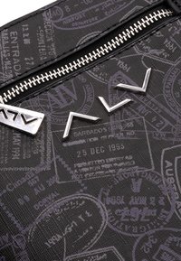 Tessuto nero con texture, dotato di hardware argentato e timbri internazionali impunturati. Il design presenta accenti angolari e una chiusura con zip.