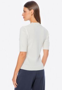 Lichtcrème trui met korte mouwen, ribbelstructuur, getailleerd ontwerp, ronde halslijn, met een kleine opening aan de achterkant. Gecombineerd met donkere broek.