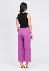 Top negro sin mangas combinado con pantalones holgados fucsias. La tela parece suave y los pantalones tienen una cinturilla elástica. Tacones visibles.