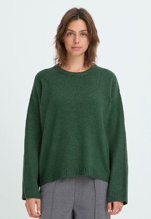 Pull en tricot vert à manches longues et coupe décontractée, doté d'un col et d'une base côtelés. Porté avec un pantalon gris.