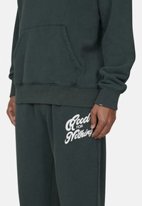 Donkergroen sweatshirt en bijpassende broek met een grote witte opdruk "Good for Nothing". Zachte stof, relaxte pasvorm, kangoeroezak op de sweatshirt.
