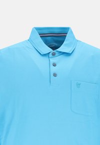 Helles blaues Polohemd mit Kragen, drei dunklen Knöpfen und einer linken Brusttasche, die ein kleines besticktes Logo zeigt. Strukturierter Stoff.