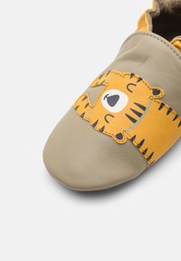 Pelēkas ādas slippers ar dzeltena tīģera sejas aplikāciju un melnām svītrām. Noapaļots pirksts un mīksta tekstūra. Ikdienišķs dizains komfortam.