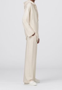 Conjunto de ropa de casa en color beige que incluye un sudadera con capucha de corte relajado y pantalones de pierna ancha. Fabricado con tela suave; incluye bolsillos laterales.