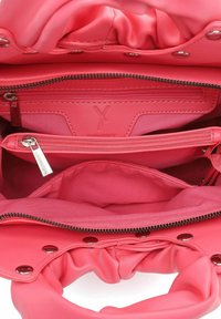 Interno della borsa in tessuto rosso con tasche con zip e texture liscia e vivace. Presenta chiusure a scatto e un delicato dettaglio del logo.
