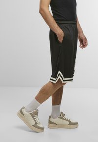 Black athletic shorts with white chevron accents, elastic waistband, side pockets; paired with cream and beige sneakers and white crew socks.