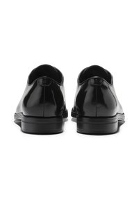 Pár leštěných černých kožených společenských bot viděných zezadu, s nízkými podpatky a jemnými švy v blízkosti horního okraje.