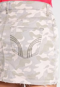 Kamouflage denim minikjol i ljusgrå och taupe. Har en bakficka med sömnadsdetaljer. Fransad fåll ger textur.