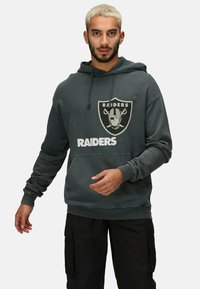 Sudadera gris con un bolsillo frontal, con el texto "RAIDERS" y el logo en blanco y negro. Tejido texturizado, capucha ajustable con cordón.