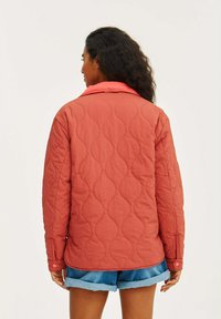 Kurtka pikowana w kolorze koralowym z kontrastowym różowym kołnierzem. Posiada klasyczny krój, zapięcia na guziki oraz teksturowany wzór na tkaninie.