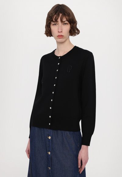 Svart stickad cardigan med rund halsringning, knappstängning och texturerad logotypdetalj på bröstet. Slät tyg med en figurnära silhuett.