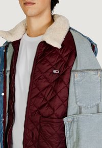 Giacca di jeans con fodera trapuntata color amaranto e colletto in eco shearling. Include una tasca frontale e dettaglio con logo marchiato sulla fodera.