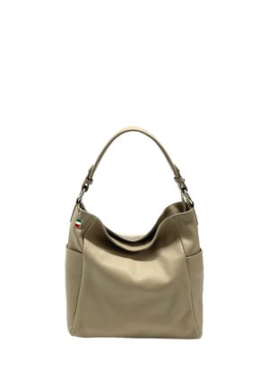 Beige leren handtas met één handvat, zijzakken en een klein vlaggetjesbedeltje dat vlak bij het handvat hangt.
