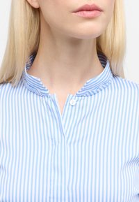 Light blue and white striped blouse with a stand-up collar, short button placket, and smooth fabric texture. No patterns or accents visible.