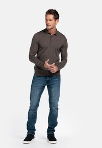 Donkergrijze polo met lange mouwen, een kraag en twee knopen, gecombineerd met lichtblauwe jeans en zwarte sneakers, staand tegen een witte achtergrond.