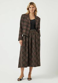 Geruit pak met een cropped, dubbelgeknoopt blazer in donkerbruin, met een bijpassende geplooide rok, beide in diepe groene en bordeauxrode tinten.