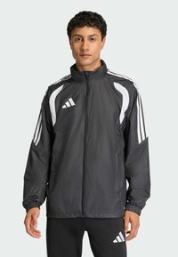 Μαύρο σακάκι windbreaker με λευκές λεπτομέρειες, κλείσιμο με φερμουάρ, ψηλό γιακά και ελαστικές μανσέτες. Περιλαμβάνει τρεις χαρακτηριστικές ρίγες στα μανίκια.