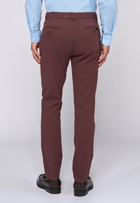 Hnědé kalhoty s úzkým střihem, vyrobené z hladké tkaniny, s dvěma zadními kapsami se zapínáním na knoflíky. Nosit s světle modrou košilí.