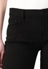 Jeans de mezclilla negra con una cintura de altura media, bolsillos frontales y cierre de botón. Presentan una textura suave y detalles de costura sutiles.