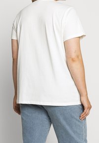 Vit bomulls t-shirt med korta ärmar, avslappnad passform och rundad hals. Bakifrån syns en jämn yta och enkel design, kombinerad med blå denimjeans.