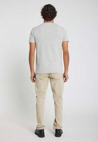 T-shirt gris à manches courtes avec un col rond, associé à un pantalon beige. La tenue présente une texture douce et un design simple.