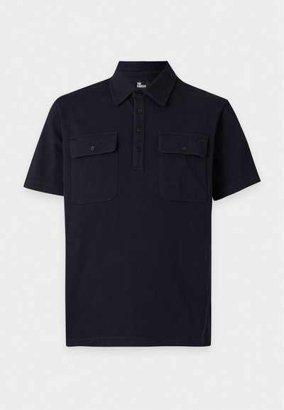 Polo noir à manches courtes avec col, patte de boutonnage à quatre boutons, et deux poches poitrine avec rabats boutonnés sur fond uni.
