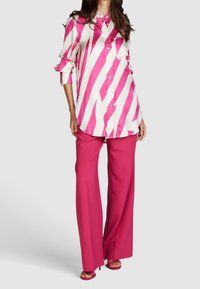 Chemise oversize rayée rose et blanche associée à un pantalon large rose vif. Tissu lisse, devant à boutons et manches retroussées.