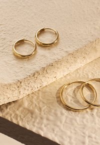 Boucles d'oreilles en or avec une finition polie, présentant une forme ronde simple et une texture lisse, exposées sur une surface neutre texturée.